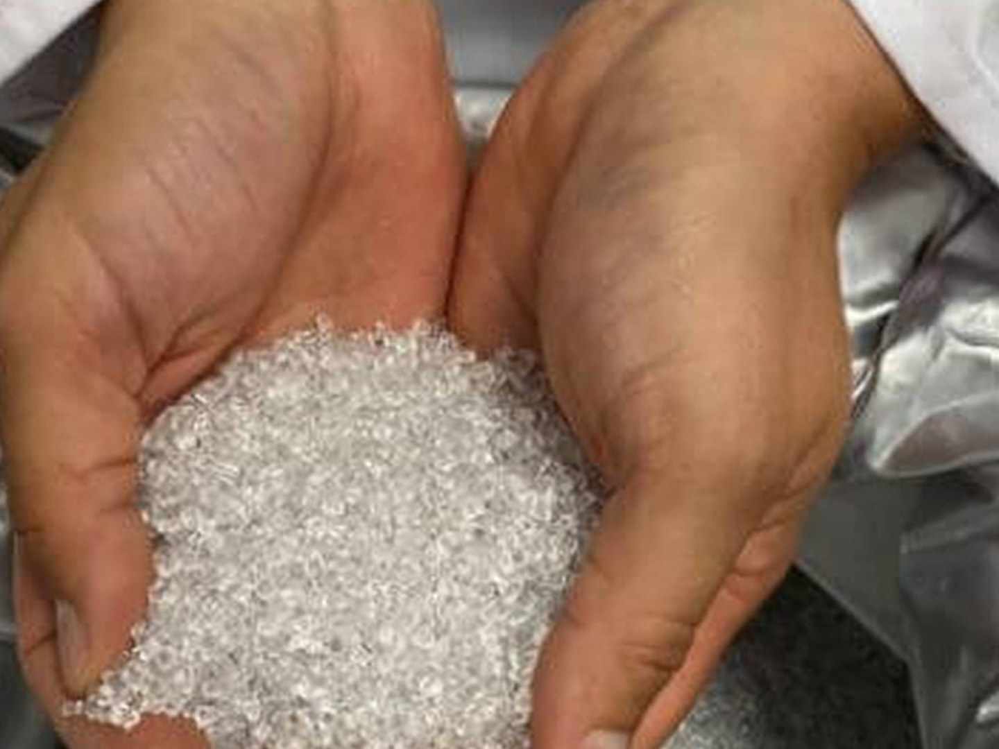 Mãos segurando pellet transparente retirado do saco de matéria-prima para impressão 3D