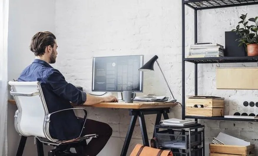Profissional trabalhando de forma remota, em estação de trabalho com computador sobre escrivaninha