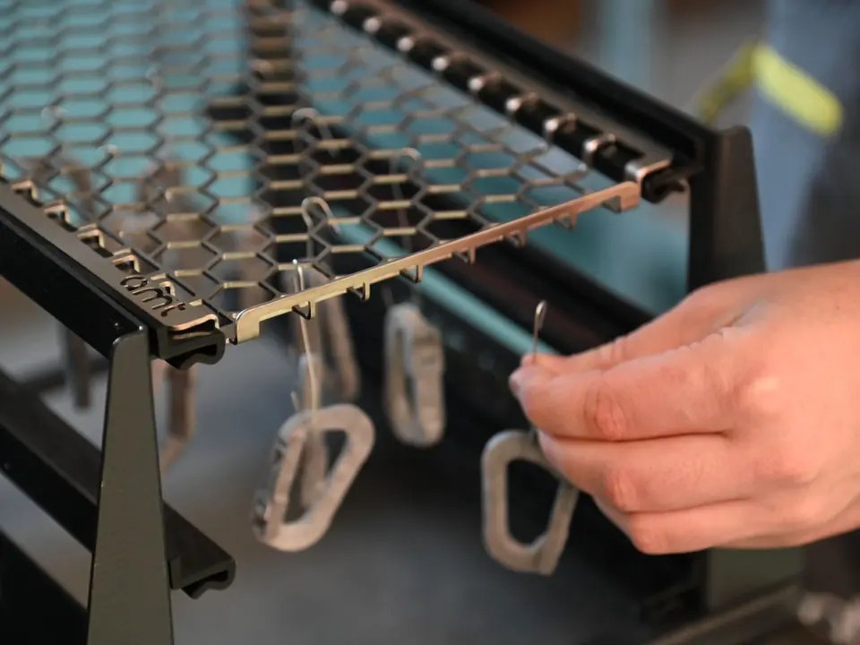 Peças impressas em pó cinza penduradas nos ganchos do rack de processamento PostPro